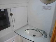 Ein ovales Waschbecken mit Wasserhabn in einer ebenen Arbeitsplatte. Links vom Waschbecken ist eine Schranktür. Die Wände sind aus weißem Kunststoff.